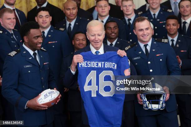 President Joe Biden shows off an Air Force football jersey presented by Air Force quarterback Haaziq Daniels and Air Force running back Brad Roberts...