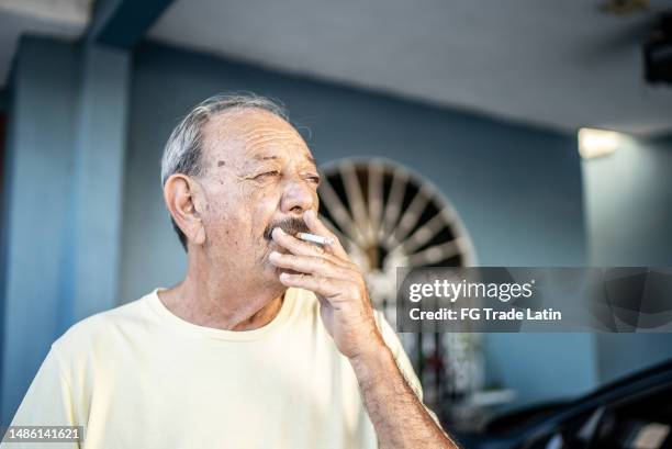 älterer mann, der zu hause eine zigarette raucht - zigarettenpause stock-fotos und bilder