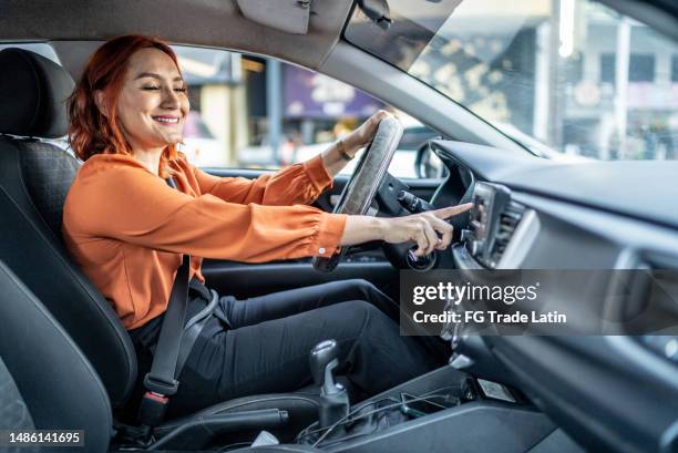 mujer adulta mediana cambiando de canción mientras conduce un automóvil - auto radio fotografías e imágenes de stock