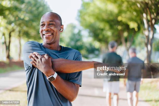retrato de un hombre maduro haciendo estiramientos en un parque público - estirándose fotografías e imágenes de stock