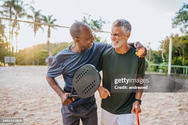 zwei ältere freunde, die beachtennis spielen - exercise 60 stock-fotos und bilder