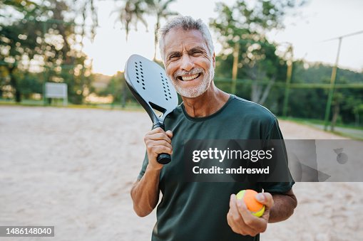 Senior man playing beach tennis looking at camera Senior man playing beach tennis looking at camera