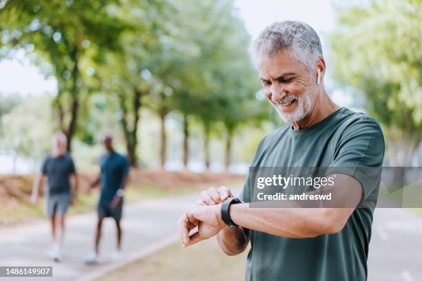 senior man runner looking at smartwatch outdoor activity - checking watch stockfoto's en -beelden