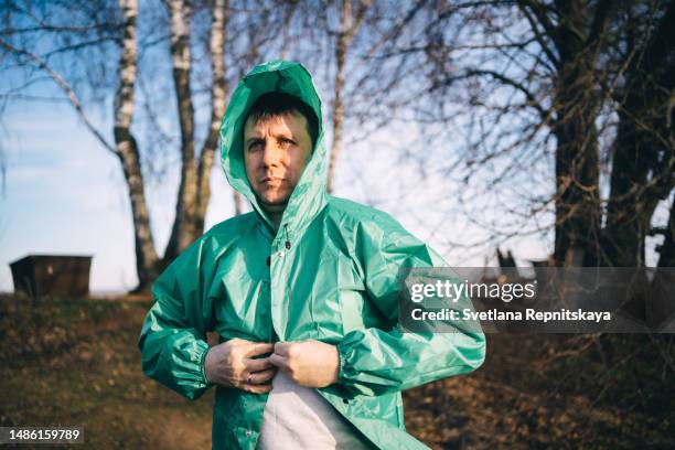 man puts on a green raincoat in a strong wind outdoor - レインコート ストックフォトと画像
