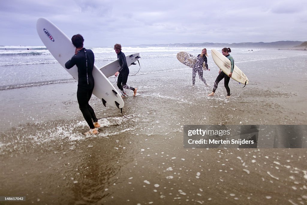 Group of surfers splashing each other while walking along shoreline.