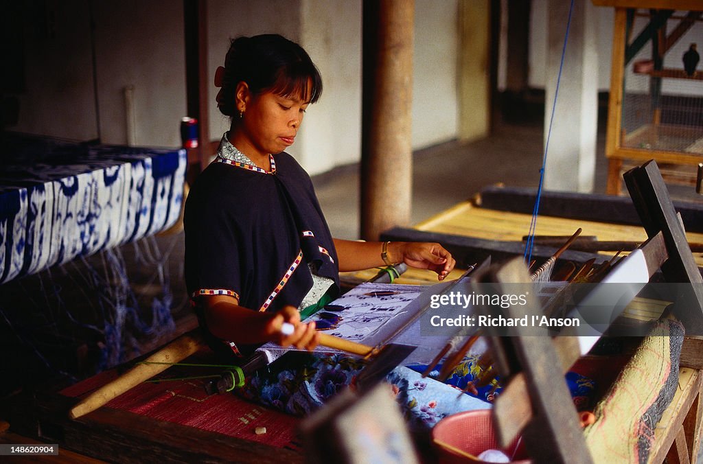 Woman weaving on traditional loom in workshop producing traditional Ikat and Songket woven fabrics.