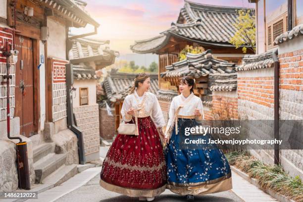 two lovely women in hanbok stroll through the traditional-style homes of seoul's bukchon hanok village. - korean hanbok stock pictures, royalty-free photos & images