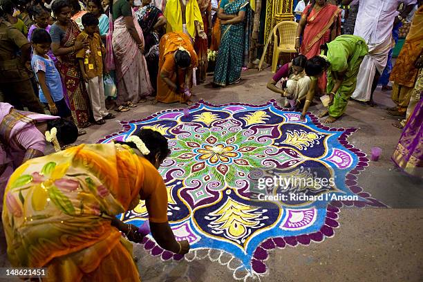 Women creating rangoli (decorative motif) with coloured powder at entrance to Sri Meenakshi Temple in preparation for festival procession.