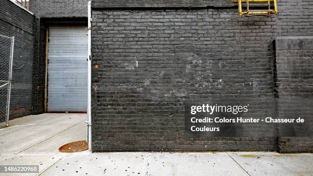 weathered brick wall painted black, closed garage door and cement floor in manhattan, new york, usa - hunter, new york stock-fotos und bilder