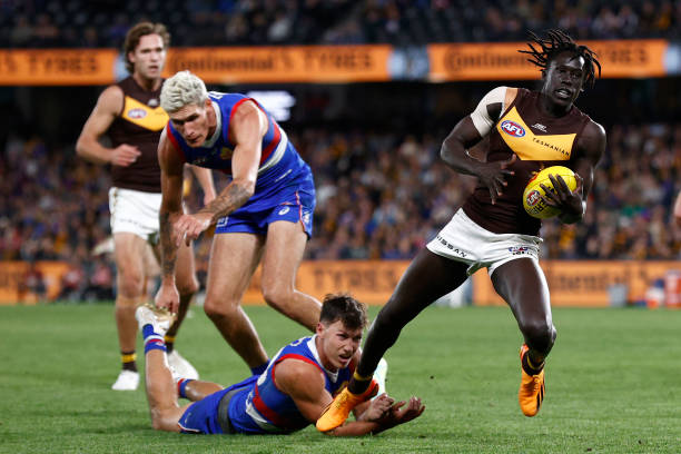 Anthony Scott of the Bulldogs trips Changkuoth Jiath of the Hawks during the round seven AFL match between Western Bulldogs and Hawthorn Hawks at...