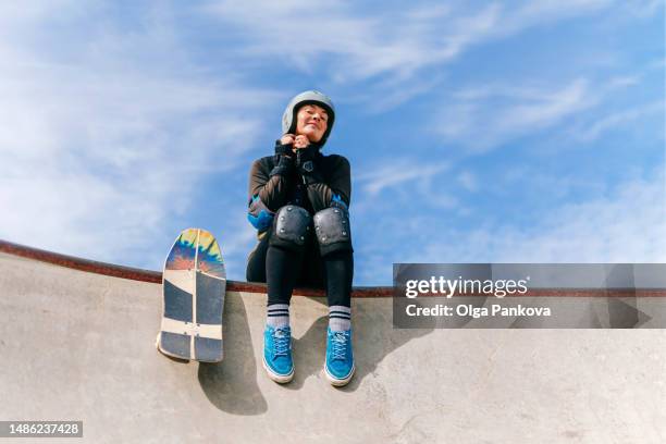 getting ready for skateboarding, woman sits on the edge of a concrete skatepark, feeling pleased with herself. - alternative lifestyle stock pictures, royalty-free photos & images