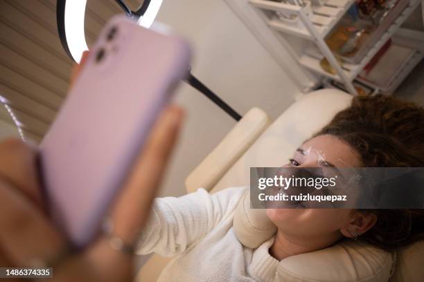 young woman taking a selfie during eyebrow lamination procedure - brow lamination stock pictures, royalty-free photos & images