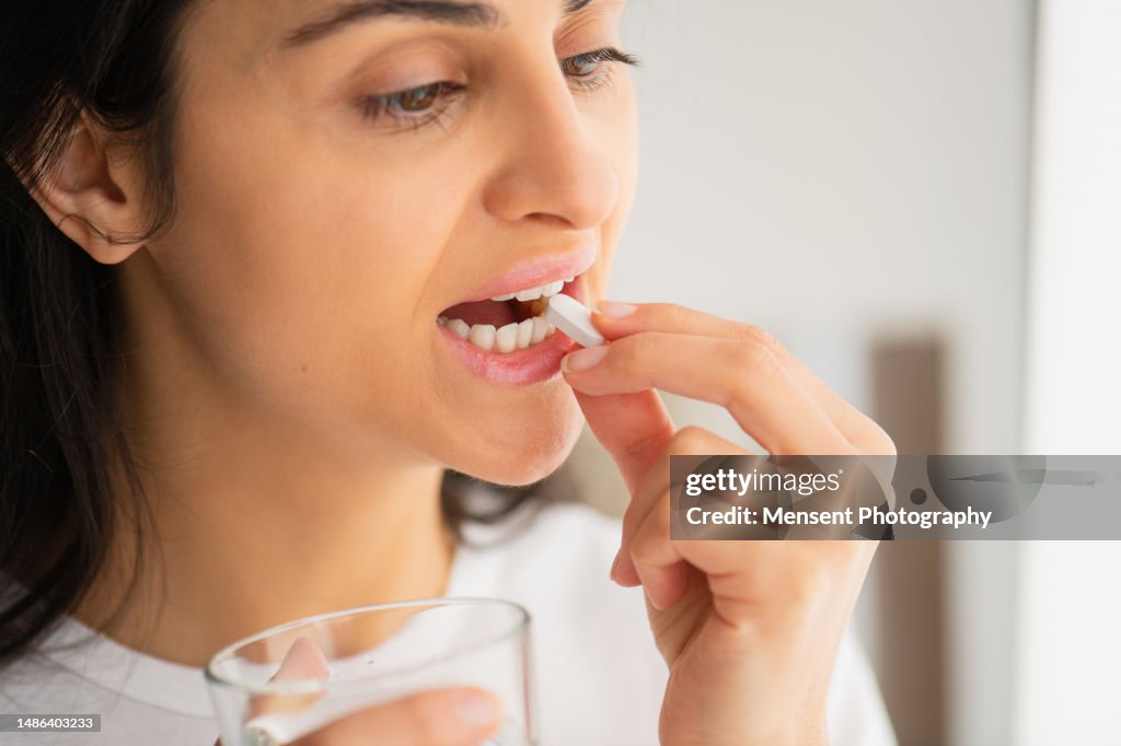 Young woman taking white pill calcium capsule, holding in mouth between teeth, Close-up