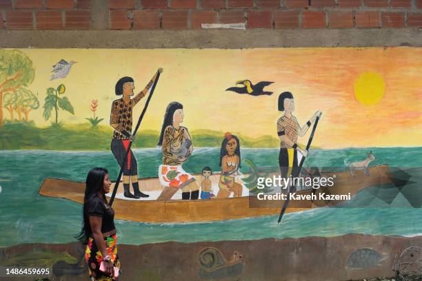 An Embera indigenous woman passes by a mural showing the indigenous of Choco Department rowing on a canoe nearby seen on January 18, 2023 in Nuqui,...