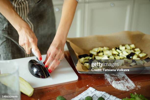 close up of female hands with red nails cutting eggplants in pieces onto baking sheet cooking vegan dish - aubergine stock pictures, royalty-free photos & images