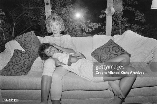 Woman, wearing an Olympic Ceremonies Olympic Drill Team t-shirt, reclining on a sofa with a woman, possibly at the athletes' village on the campus of...
