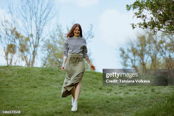 beautiful mature woman walking down green hill smiling on sunny day - running shoes sky ストックフォトと画像