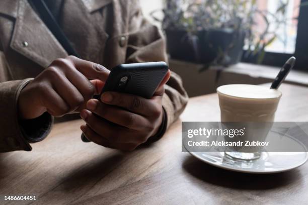 a black man, a freelancer holds a mobile phone in his hands, in a cafe, office, coworking. job search. the entrepreneur corresponds on social networks with clients, offers services. dating in apps and communities. business concept, customer engagement. - romance fraud stock pictures, royalty-free photos & images