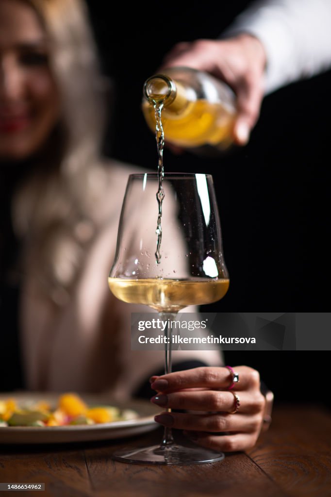 Waiter serving white wine to a beautiful woman