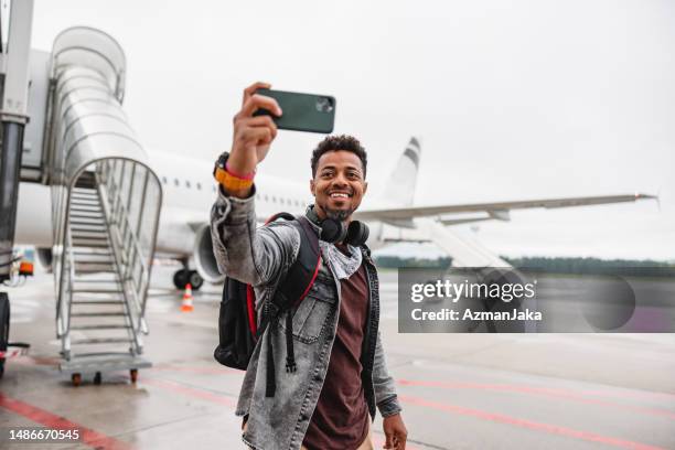 schwarzer mann macht ein selfie vor dem flugzeug - passenger boarding bridge stock-fotos und bilder