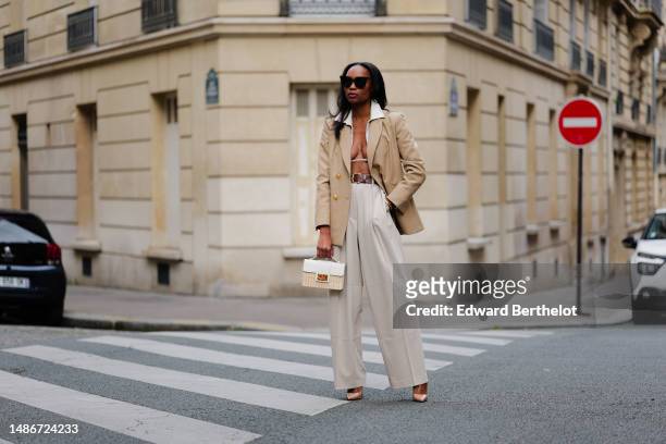 Emilie Joseph wears black large sunglasses, small earrings, a white linen V-neck / cropped laces shirt, a beige with gold buttons blazer jacket, a...