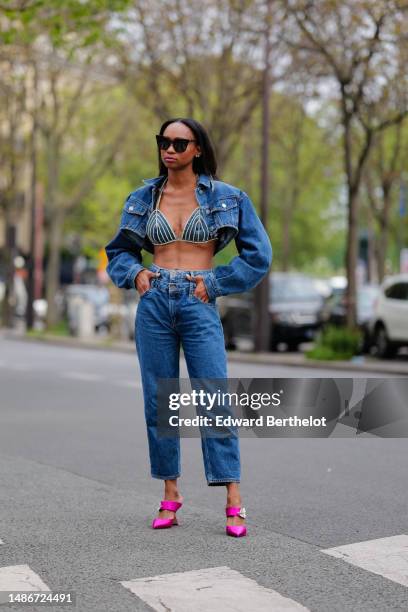 Emilie Joseph wears black large sunglasses, small crystal earrings, a navy blue denim cropped cargo jacket, a matching navy blue denim with...