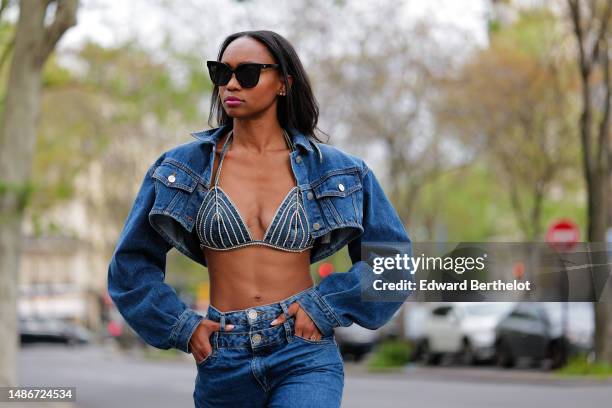 Emilie Joseph wears black large sunglasses, small crystal earrings, a navy blue denim cropped cargo jacket, a matching navy blue denim with...