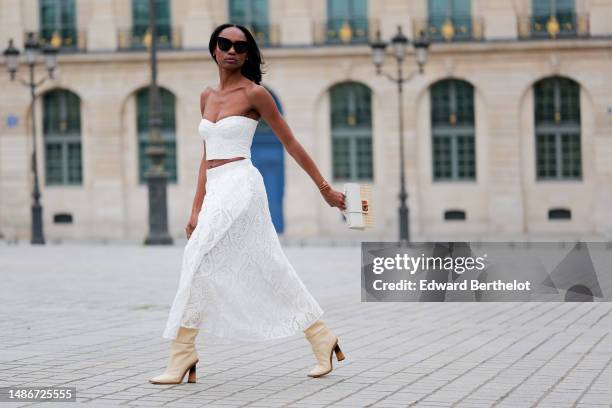 Emilie Joseph wears black large sunglasses, micro rhinestones earrings, a white embossed lace pattern heart shoulder-off / cropped top, a matching...