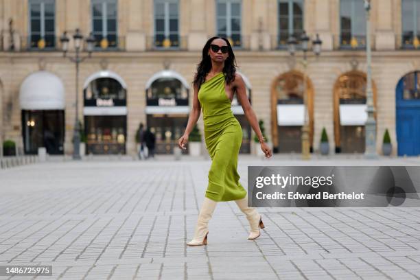 Emilie Joseph wears black large sunglasses, micro crystal earrings, a green satin / silk asymmetric one strap shoulder midi tube dress, gold...