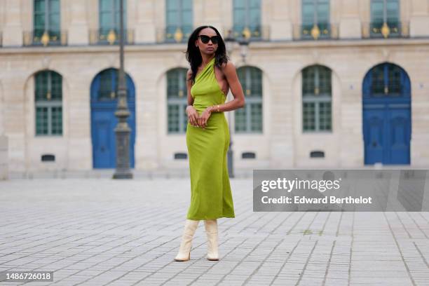 Emilie Joseph wears black large sunglasses, micro crystal earrings, a green satin / silk asymmetric one strap shoulder midi tube dress, gold...