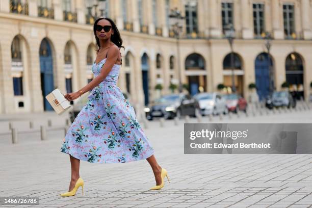 Emilie Joseph wears black large sunglasses, crystal earrings, a pale blue with red / green / navy blue / beige flower print pattern heart neck /...