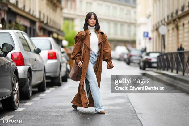 Heart Evangelista wears a white fluffy turtleneck / asymmetric cropped / backless pullover, a pale brown shiny leather oversized long jacket, a dark...