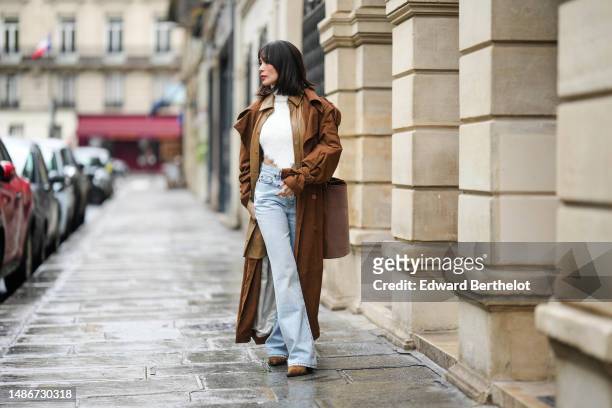 Heart Evangelista wears a white fluffy turtleneck / asymmetric cropped / backless pullover, a pale brown shiny leather oversized long jacket, a dark...