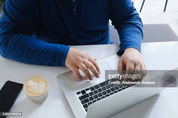 a man, a businessman, a manager uses a laptop in a cafe, office or at home. entering text on the laptop keyboard, with your hands. next to a mobile phone, a cup of tea. search for information on the internet. business concept, freelance work, training. - addiction mobile and laptop stockfoto's en -beelden