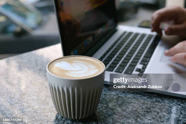 a man, a businessman, a manager uses a laptop in a cafe, office or at home. entering text on the laptop keyboard, with your hands. next to a mobile phone, a cup of tea. search for information on the internet. business concept, freelance work, training. - addiction mobile and laptop stockfoto's en -beelden