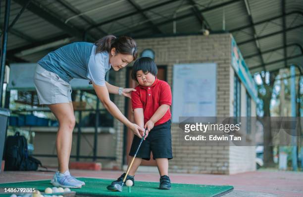 asian chinese female coach guiding young boy in driving range golf lesson holding golf club - golf lessons stock pictures, royalty-free photos & images