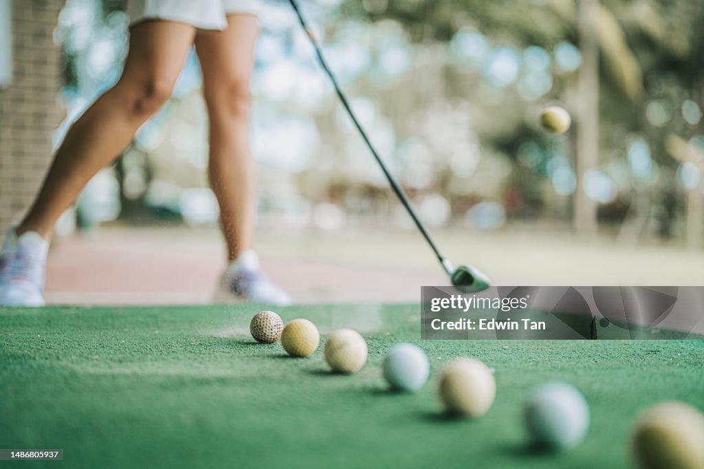 Low section asian chinese female golfer practicing golf swing at driving range