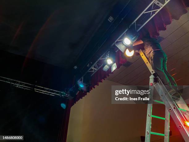 junger männlicher lichttechniker, der auf einer leiter steht und scheinwerfer installiert - bühnenbild stock-fotos und bilder