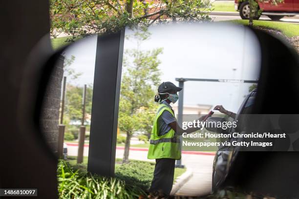 Drive thru worker, wearing a protective mask and gloves, takes a payment for an order on Saturday, April 11, 2020 in Richmond. With restaurants...