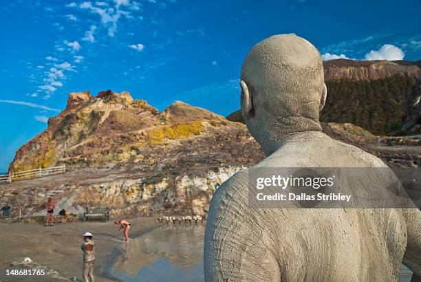 mud-covered man observing therapeutic volcanic thermal mud pool, levante beach. - mud therapy stock pictures, royalty-free photos & images