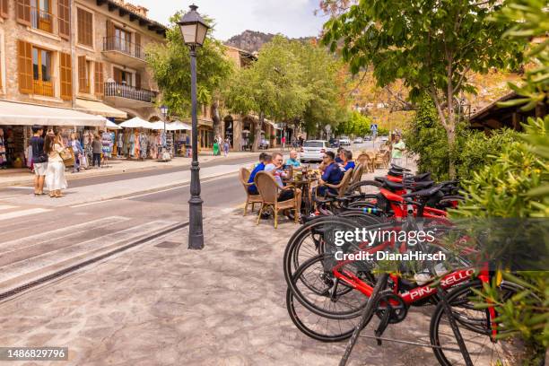 cyclist team sitting together in an outdoor cafeteria on the main street in the famous village valldemosa - mountain village stock pictures, royalty-free photos & images