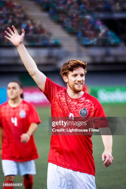 confident male soccer player excitedly waves toward fans before international match - pre game huddle stock pictures, royalty-free photos & images