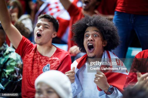 stunned young adult sports fans in bleachers have a jaw dropping reaction to their soccer team scoring an unexpected goal - surprise stadion stock-fotos und bilder