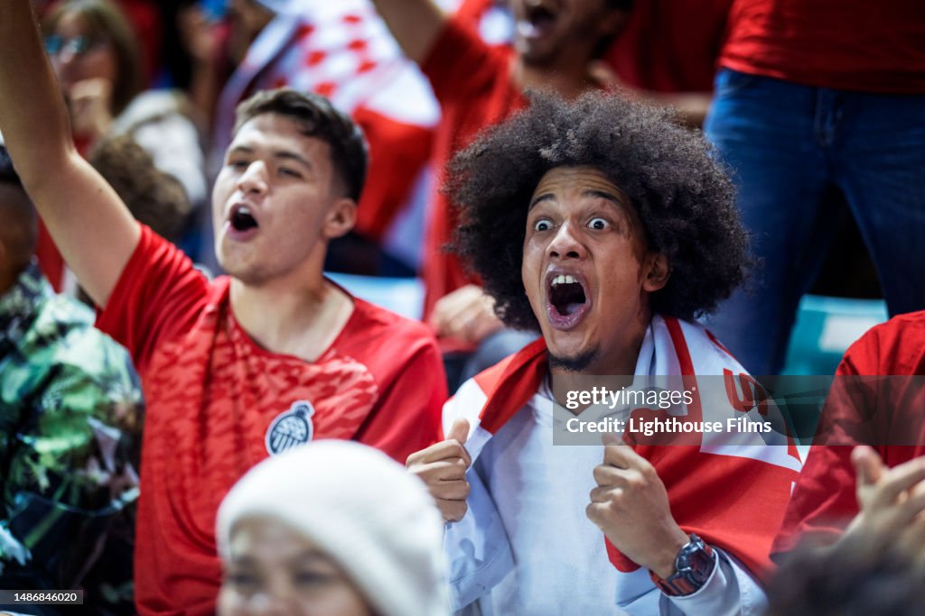 Stunned young adult sports fans in bleachers have a jaw dropping reaction to their soccer team scoring an unexpected goal