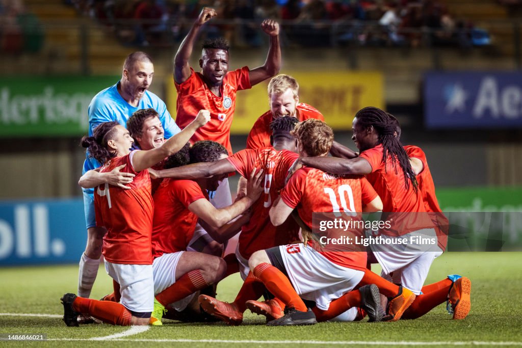 Passionate team of professional male soccer players surround their teammate while celebrating a tournament win