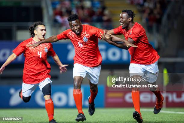professional soccer players excitedly run up to their teammate while cheering to celebrate scoring a goal - midfielder soccer player stockfoto's en -beelden