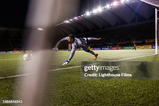 Action rear view shot of a male professional soccer goalie diving to stop a goal during a live international game Action rear view shot of a male professional soccer goalie diving to stop a goal during a live international game