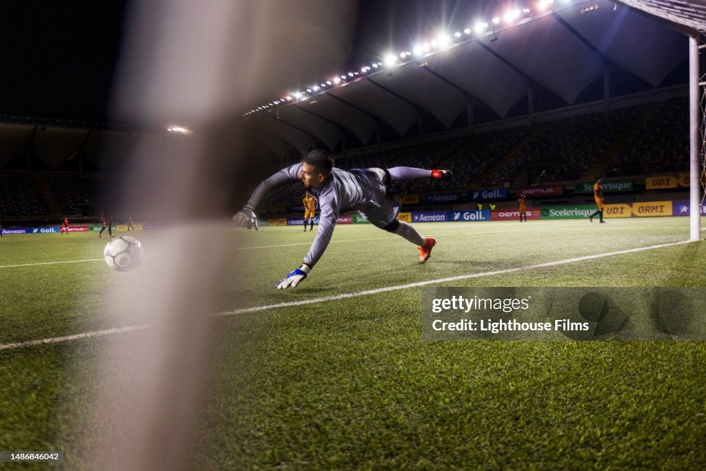 Action rear view shot of a male professional soccer goalie diving to stop a goal during a live international game