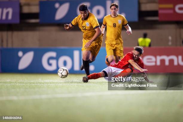 international male soccer player slide tackles opponent to kick ball away and trips him - overtreding stockfoto's en -beelden