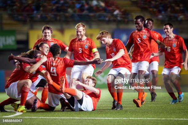 ecstatic team of male soccer players run together and embrace their striker teammate to celebrate a goal - time de futebol imagens e fotografias de stock